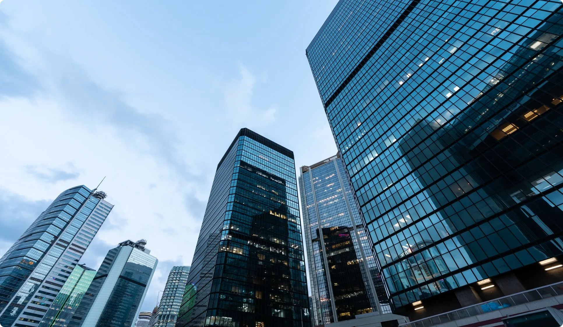 Glass office towers in Hong Kong seen from street level against a blue sky